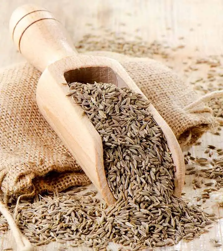 Whole cumin seed in a wooden scoop on a burlap sack
